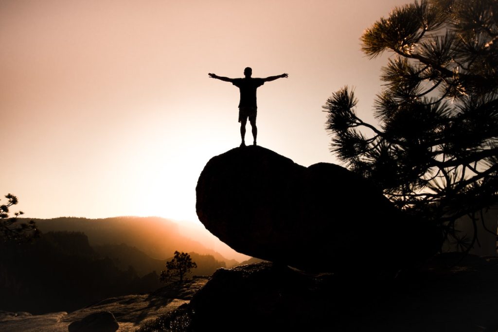 person stood doing the power pose stretching arms wide open at sunset on a rock