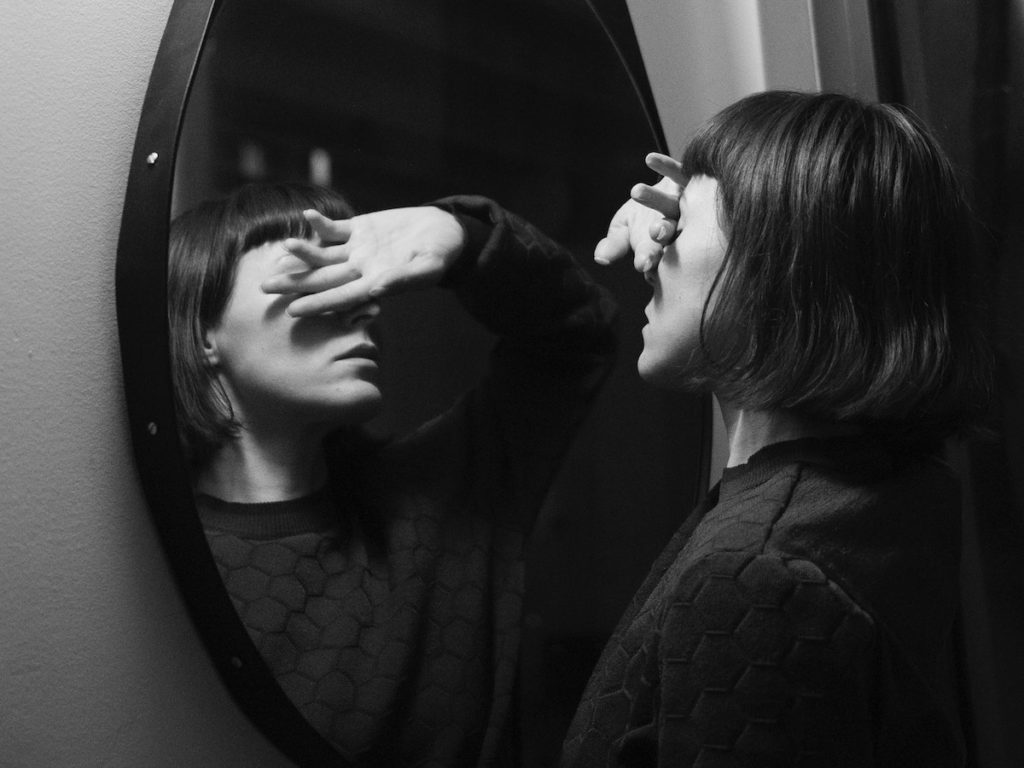 are our mirrors ruining our lives blaxck and white photo of woman looking sad in the mirror