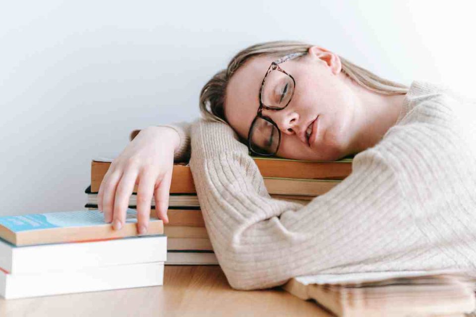 Woman sleeping at table resting her head on a pile of books: Dealing with the Physical Signs of Stress by Bodyshot Performance