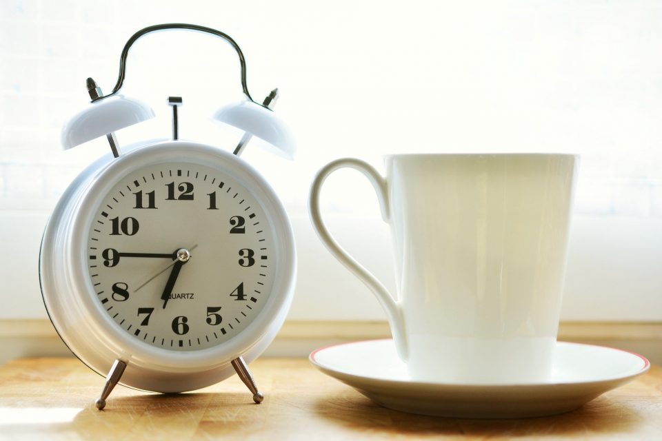 A white alarm clock and white cup and saucer on a wooden table