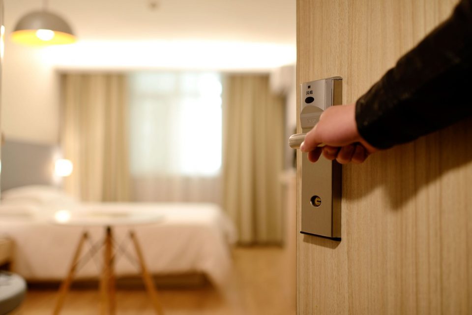 A hand opening a door into a hotel room