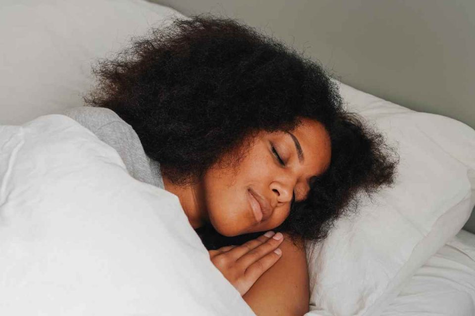 Woman sleeping in bed with a smile on her face. The connection between sleep and mood and how to improve both by Bodyshot Performance.