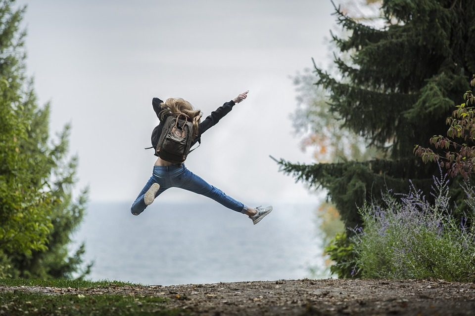 A person jumping in the air with excitement, facing a view of trees and water